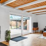Wohnbereich mit Kamin, Glasfront und Holzboden. Fernseher, Sofa und Küchenzeile sichtbar.