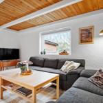 Wohnzimmer mit grauem Sofa, Holztisch und Fernseher. Holzdecke und Fenster mit Blick nach draußen.