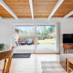 Wohnraum mit Holzdecke, Kamin, TV und Blick auf Terrasse mit Garten.