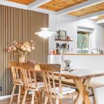 Essbereich mit Holztisch, Stühlen und Holzwand. Küche mit Küchenschränken und Fenster.