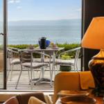 Terrace with table and chairs offers sea view. In foreground lamp and seating furniture.