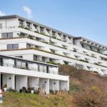 Modern multi-family house with terraces and green areas on a slope.