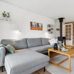 A living room with gray sofa, wooden table, and wood stove against stone wall.
