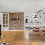 Living and dining area with fireplace, hardwood floor, and stone wall. Kitchen with dining table and window.