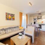 Wohn- und Essbereich mit Sofa, Tisch und Küche im Hintergrund.