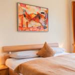 Ein Bett mit Kissen und Bettwäsche. An der Wand hängt ein Bild. Vor dem Fenster hängen Vorhänge.