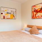 Schlafzimmer mit Bett, Kissen und zwei Wandbildern.