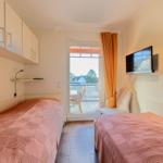 Zwei Betten, TV, Balkon mit Sitzgelegenheit und Küchenzeile im Zimmer.