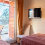 Zimmer mit Balkon, Bett, Fernseher und Wandbild.