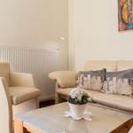 Wohnzimmer mit Sofa, Sessel und Glas-Tisch. Wandbild und Heizkörper sichtbar.