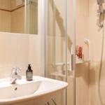 Badezimmer mit Dusche, Waschbecken und Spiegel. Handtücher und Pflegeprodukte sind vorhanden.