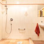 Dusche mit Handbrause, Spiegel und Waschbecken mit Handtuch.