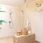 Dusche mit Pflanze, Holzwaschbecken und Statue. Tür zum Frischluftbereich.