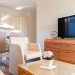 Wohnbereich mit TV, Couch und Küchenbereich im Hintergrund.