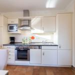 Küche mit weißen Schränken, Edelstahlspüle, Herd und Dunstabzugshaube.