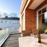 Terrasse mit Tisch, Stühlen, Wein und Blumen. Blick auf Haus und Bäume.