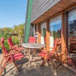 Terrasse mit Holztisch und roten Stühlen, angrenzend an ein Haus mit Glasfront.