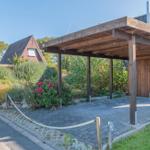 Holzüberdachung mit Sitzbereich, umgeben von Blumen und Grünflächen.