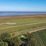 Weitläufiges Landschaftsbild mit Feldern, Wegen und Meeresufer unter klarem Himmel.