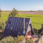 Haus mit Dachterrasse, umgeben von Feldern und Bäumen unter blauem Himmel.