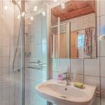 Badezimmer mit Dusche, Waschbecken und Spiegel. Holzdecke und Fliesenwand.