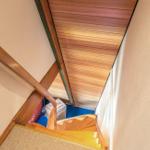 Holzgetreppe mit Geländer führt zu einem Dachboden mit Holzdecke.