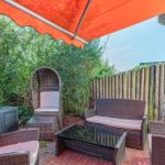 Terrasse mit Sitzgruppe unter orangefarbenem Sonnenschutz, umgeben von Grün und Holzzaun.