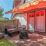 Terrasse mit Rattanmöbeln und orangefarbenem Markisenüberdachung. Hinterhof mit Holzzaun und Grünfläche.
