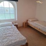 Zwei Einzelbetten mit weißen Bettwäschen und Holzrahmen. Ein großes Fenster mit Blick auf Grünfläche.