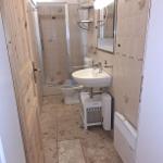 Badezimmer mit Dusche, Toilette und Waschbecken. Fliesen und Holztür sichtbar.