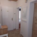 Eingangsbereich mit Holztür, Spiegel und Kleiderhaken. Durchgang zu Schlafzimmer und Holzschrank.