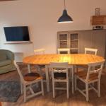 Essbereich mit Holztisch, weißen Stühlen und Fernseher an der Wand.