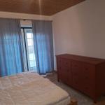 Schlafzimmer mit Bett, Schrank und Fenster mit Vorhängen.