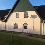 Haus mit weißem Putz, grünem Dach und arkgelbem Eingangsbereich.