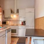 Küche mit weißer Einbauküche, Spüle, Herd und Esstisch mit Bank.