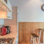 Küche mit Arbeitsplatte, Herd und Tisch mit Stühlen an Holzwand.