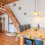 Esszimmer mit Tisch, Stühlen und Holztreppe zur oberen Etage.
