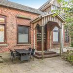 Rotes Backsteinhaus mit Holzveranda und Außentisch. Umgeben von Grünflächen.