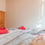 Zwei Betten mit gemusterten Bettwäsche und roten Handtüchern. Holztür und Wand sichtbar.