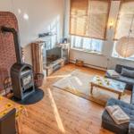 Wohnzimmer mit Sofa, Kamin und Holzboden. Fenster mit Jalousien und Esstisch mit Sonnenblumenmuster.