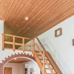Holzgetäfelte Decke, Treppe zu einer Galerie mit Holzgeländer und zwei Wandregalen.