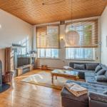 Wohnzimmer mit Holzboden, Sofa, Kamin und Fenstern mit Jalousien.