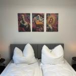 Zwei Betten mit weißen Kissen und Decken, Wandbilder mit Entenmotiv und Bitcoin, Nachttische mit Lampen.