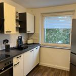 Küche mit Arbeitsplatte, Spüle, Herd und Kühlschrank. Fenster mit Jalousie und Blick auf Bäume.