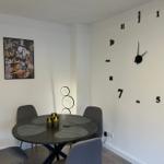 Runder Tisch mit Stühlen, Wanduhr mit Ziffern und Bild an der Wand.