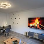 Wohnzimmer mit Esstisch, Wanduhr und Fernseher mit Kaminbild.