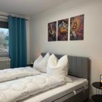 Schlafzimmer mit Bett, Wandbildern und Fenster mit Blick auf Dach und Bäume.