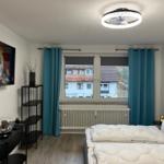 Schlafzimmer mit Bett, TV und Fenster mit Blick auf Gebäude.