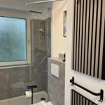 Badezimmer mit Dusche, Toilette und Fenster mit getöntem Glas.