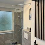 Badezimmer mit Dusche, Fenster und Holzpaneelen an der Wand.